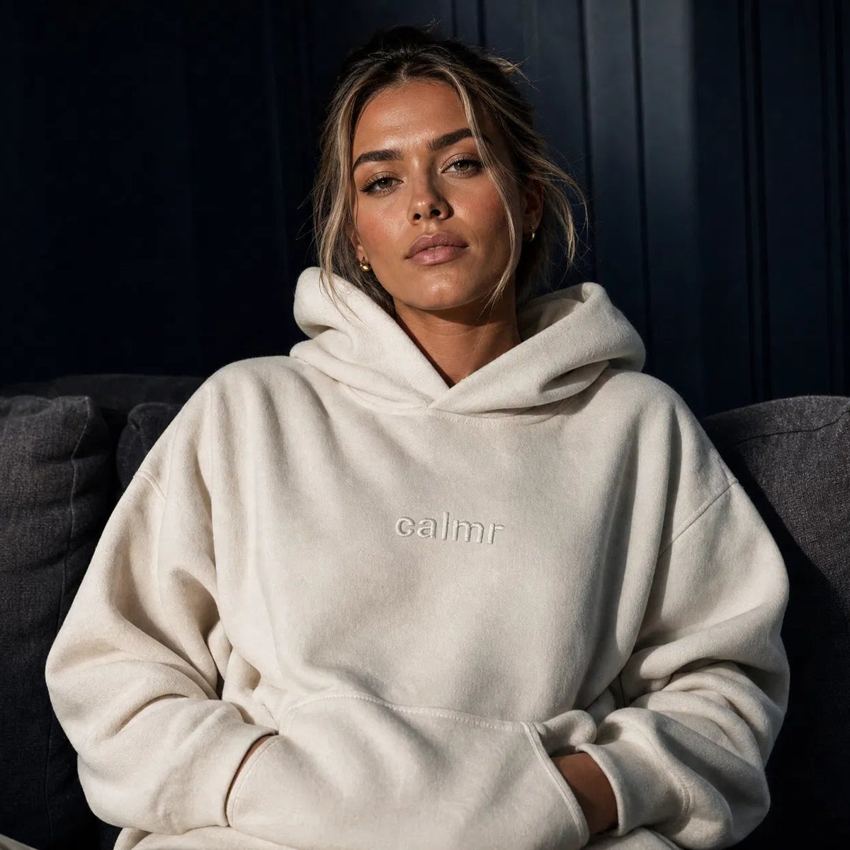 Person wearing a white hoodie with 'calmr' text, sitting on a dark couch.